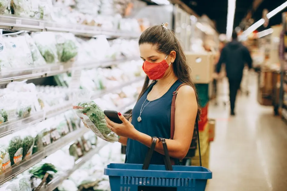 Shopper checking a smartphone app while grocery shopping, illustrative stock photo